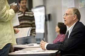 Official seated at a table taking questions from individuals and handing out information forms.