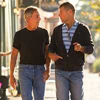 Photo of two men walking down the street while talking. The men are facing each other.