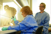 	CDC Microbiologists Olga Kosoy and Amy Lambert, in blue protective gear, working together in the lab. 