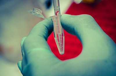 	A blue gloved hand holding an Eppendorf Tube being filled by a pipette.