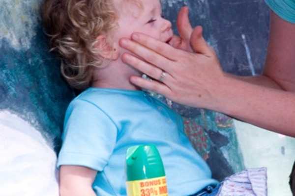 A mother applying insect repellant to a toddler's face with her hands.