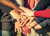 Photo of many people with their hands in the middle of a circle together.