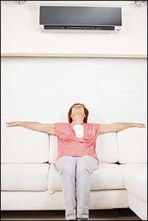 A woman sitting on a couch under an air conditioner, enjoying the cool breeze