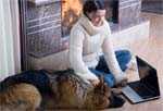 Woman sitting in front of fireplace with dog and laptop