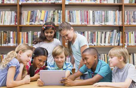 children in a library gathered around a laptop computer