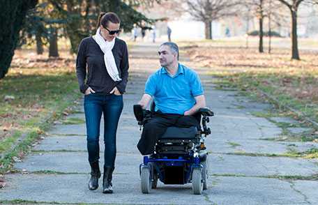 Man in an electric wheelchair strolling in a park with a friend