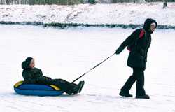 Kid pulling another kid on a sled in snow