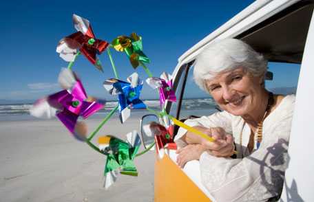 Woman holding pinwheel out window of camper van on beach