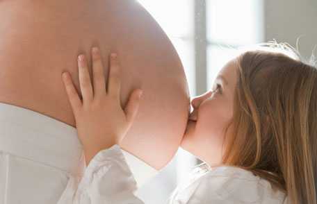 Young daughter kissing pregnant mother's belly