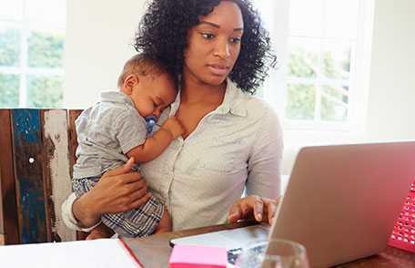 Mother holding baby and looking at laptop