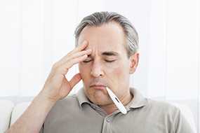 Man with thermometer in his mouth while holding his head.