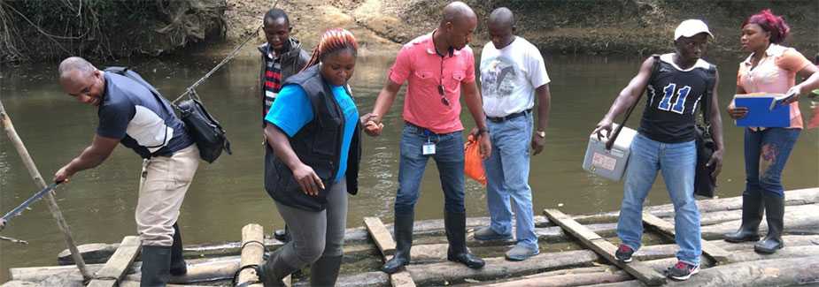 Liberian disease detective trainees carefully cross a river on a long raft to reach remote settlements.