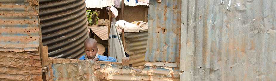 A young boy looks out from behind a wall of corrugated metal in the Kibera informal settlement in Nairobi, Kenya. The CDC is conducting the International Emerging Infections Program in Kibera and Kisumu, in western Kenya. 2009