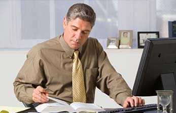 	Man looking at a book while typing on a keyboard.