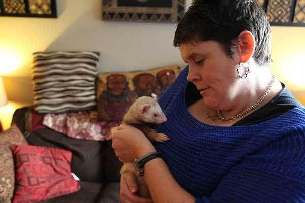 Woman cuddles pet ferret.