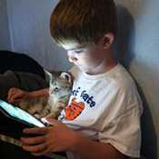 Boy sits with kitten while he looks at iPad.