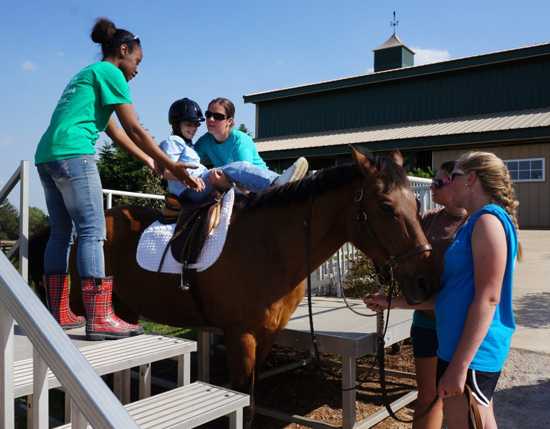 Group of volunteers helping a child onto a horse