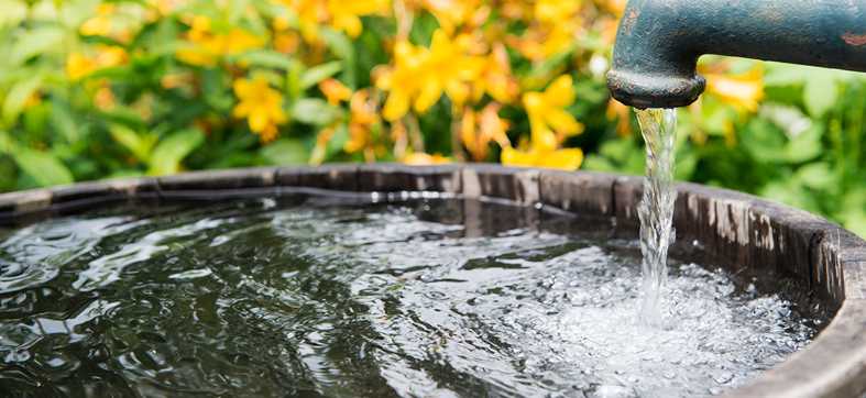 an outdoor spigot with water running into a wooden cistern