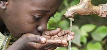 	Young boy drinking from a faucet