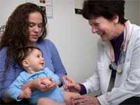 This photograph showed an infant being held by his mother while receiving an intramuscular vaccination in his left thigh muscle. A qualified nurse was administering the vaccination while stabilizing the injection site.