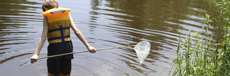 photo: boy standing in a pond wearing a life jacket