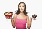 Woman holding a piece of cake in one hand and a salad in another. 