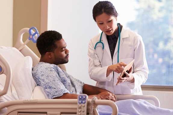 a man in a hospital bed, speaking with his doctor