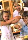 A girl cracks open an egg while her mother and brother look on.