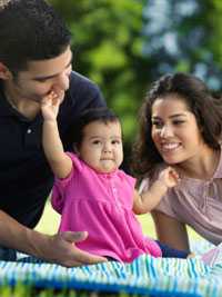 Mom and dad sitting with baby on blanket.