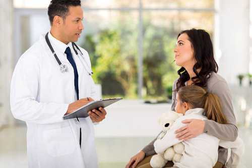 Doctor talking to a mom and a little girl holding a teddy bear.