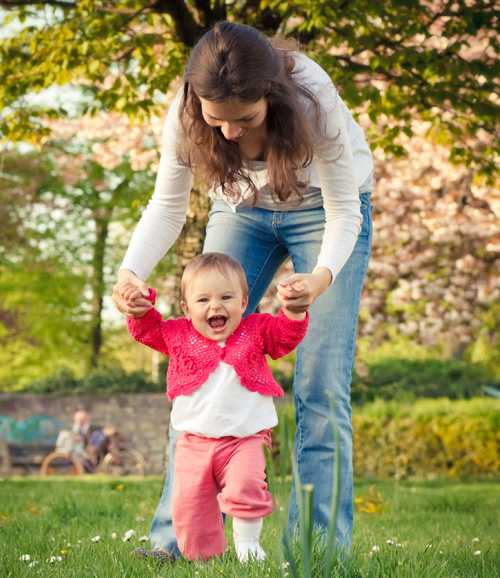 Mom helping her toddler walk in a park