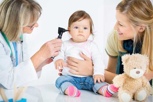 Doctor examinando el oído del niño con la madre sonriendo.