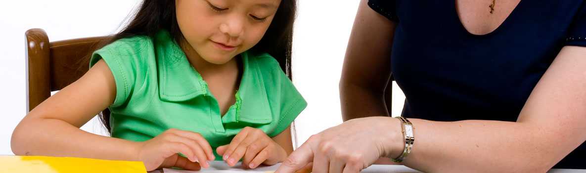 A young child sitting at a desk with her teacher