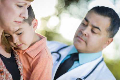 Foto de una madre cargando a su hija mientras que el doctor la examina.