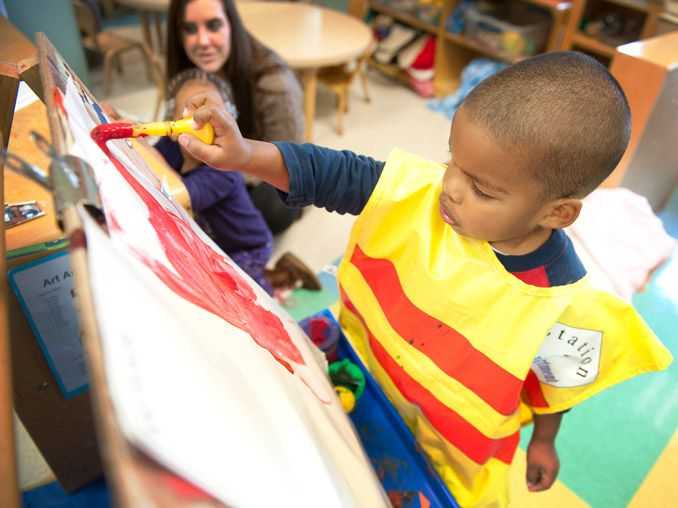 A childcare provider watches as a young boy paints.