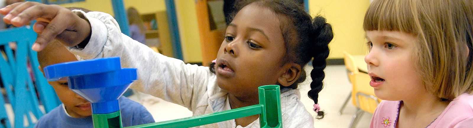 Two girls play with a marble toy.