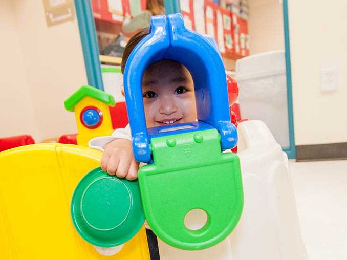 Un niño espía por un buzón de juguete y sonríe.