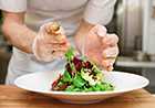 Close up photo of gloved hands preparing a salad.