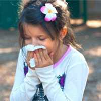 A girl covers her nose and mouth wiht a tissue while sneezing.