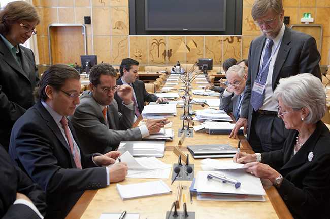 Two government officials sign a declaration while sitting opposite of one another. 