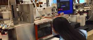 Thumbnail image of a woman leaning in to see a screen as she works in a cdc laboratory.