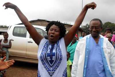 An african woman and doctor standing in a group of people. The woman has her arms raised in celebrating