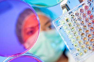 Photo of female scientist with colored petri dishes and testing equipment