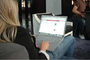  A young-looking woman with long blond hair sits on a chair in what looks to be an internet café.