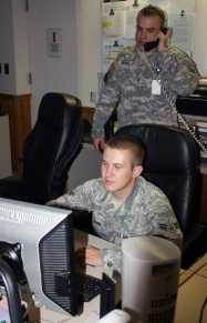 one man talking on the telephone and another working at a computer