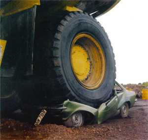 Large dump truck driving over smaller vehicle