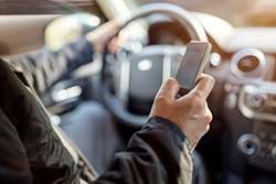 	driver at wheel with cell phone in hand