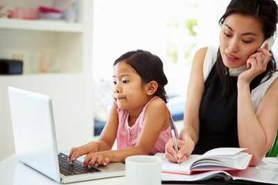 Child using laptop and woman talking on phone and writing in book.