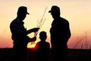 Two men and a child silhouetted in the sunset on a family farm