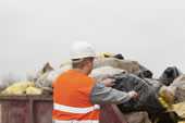 	Back view of man putting bags of garbage into dumpster